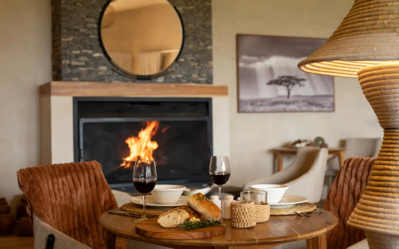 Dining table set for two by fireplace with wine and bread, Osonjoi Lodge, Ngorongoro Crater, Tanzania
