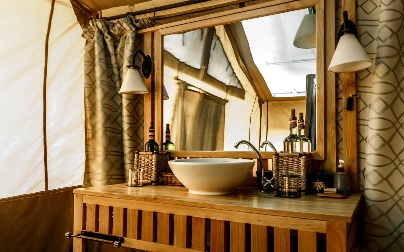 Luxury bathroom vanity with round basin and wine bottles in woven baskets, Porini Lion Camp, Maasai Mara, Kenya