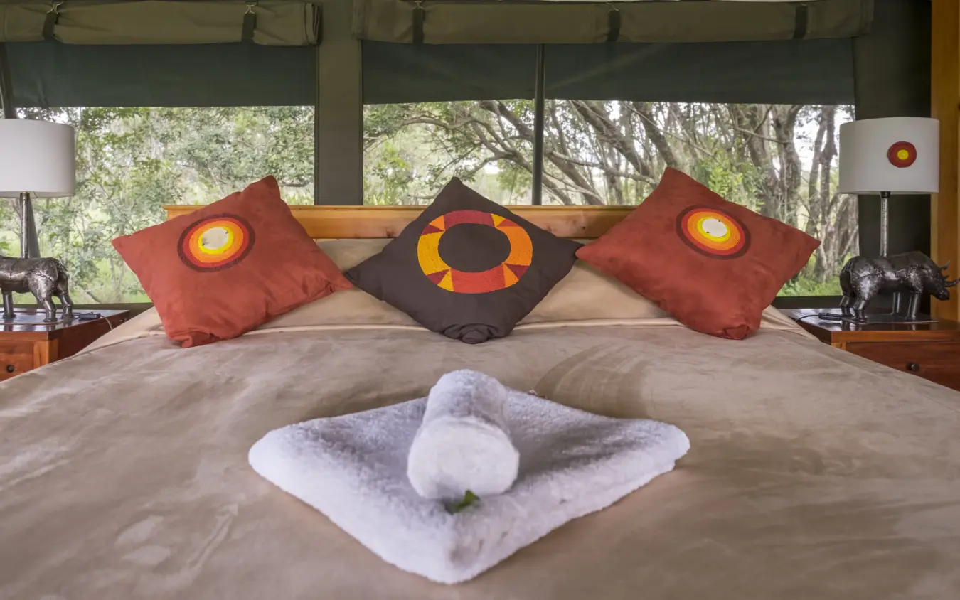Bedroom with decorative pillows and rolled towels on bed overlooking trees, Porini Rhino Camp, Laikipia Highlands, Kenya