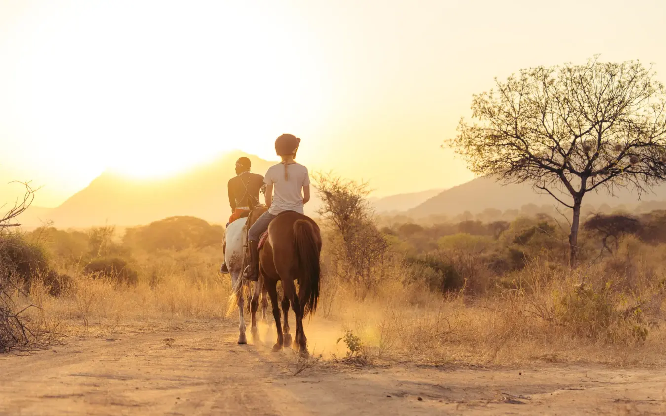 Two riders on horseback on dusty trail through savanna at sunset, Reteti House, Northern Kenya, Kenya
