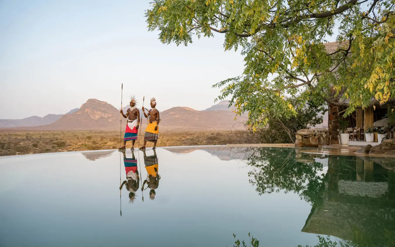 Indigenous warriors with spears reflected in infinity pool overlooking savanna, Reteti House, Northern Kenya, Kenya