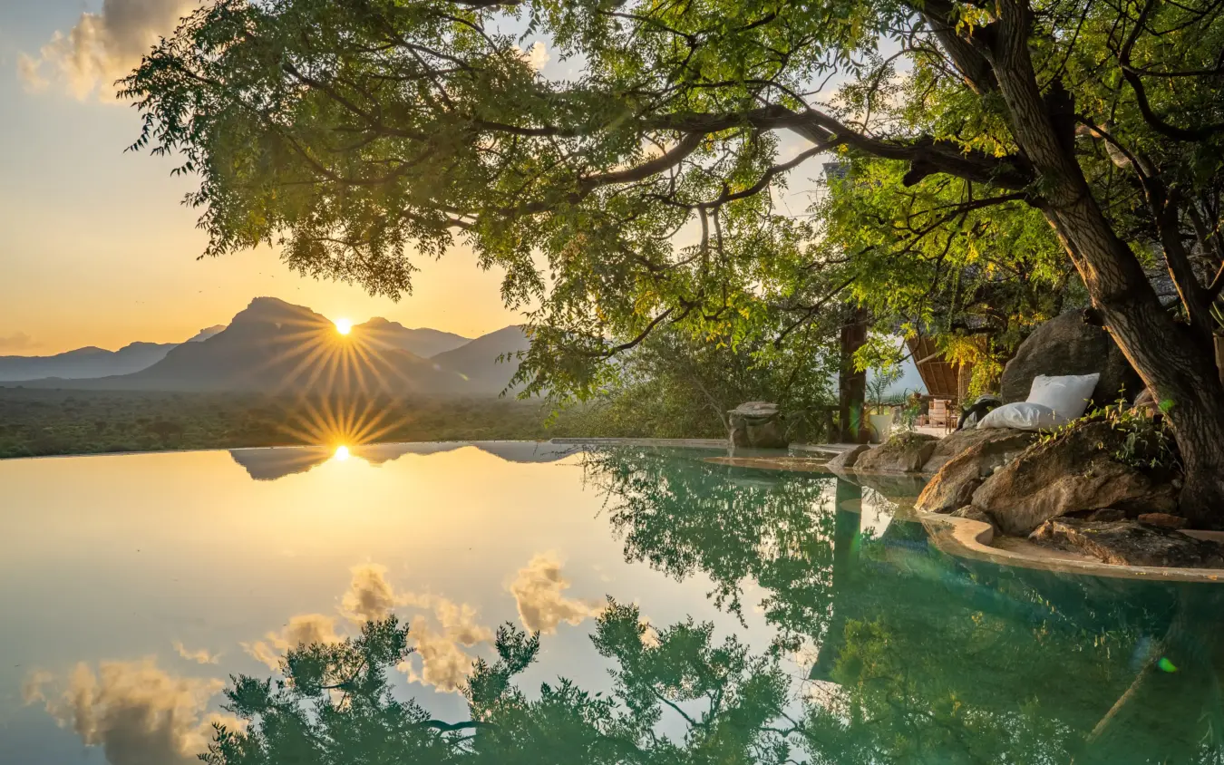 Emerald pool with mountain backdrop and large tree at sunrise, Reteti House, Northern Kenya, Kenya