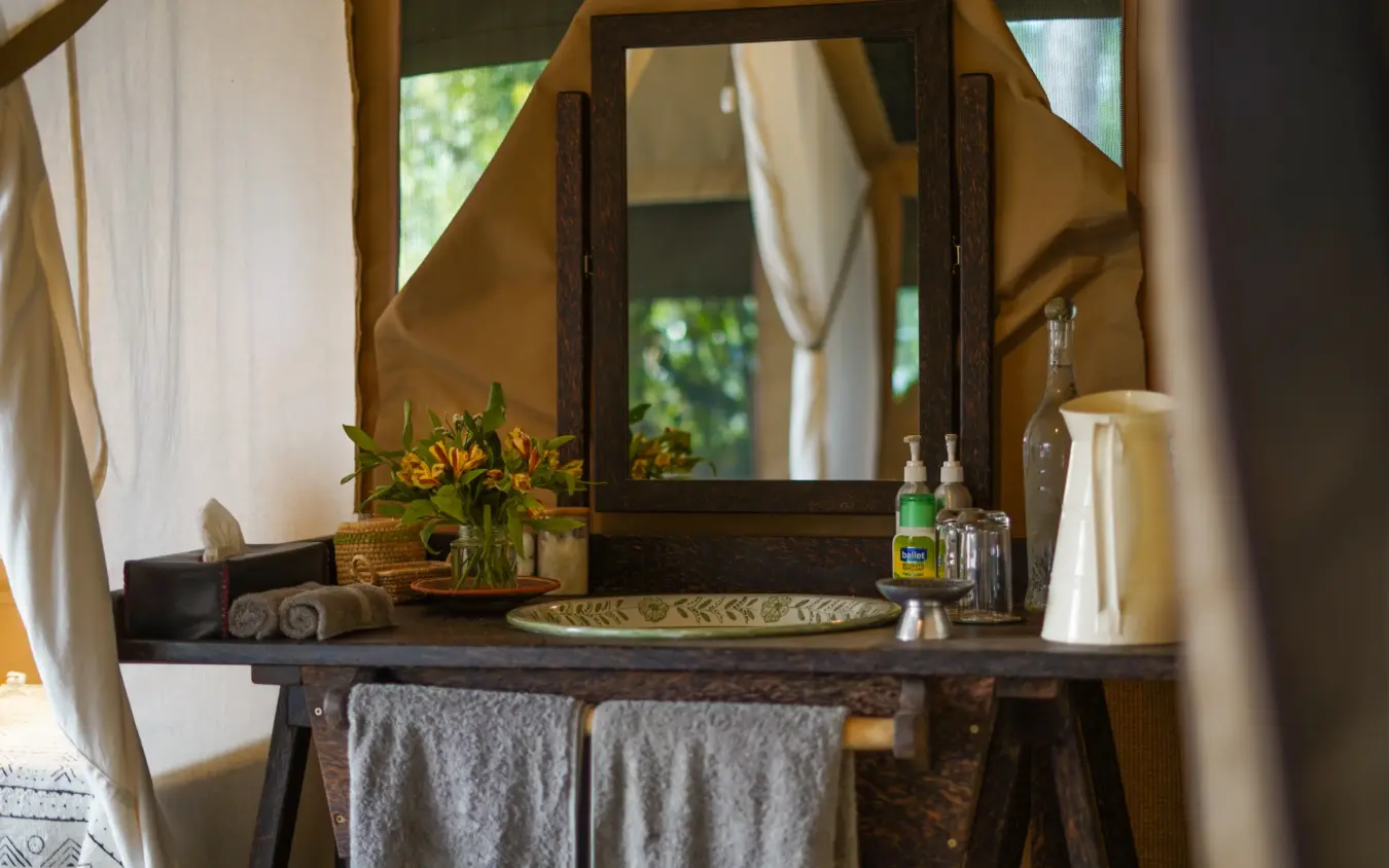 Bathroom vanity with mirror and flowers in natural daylight, Roca River Camp, Maasai Mara, Kenya