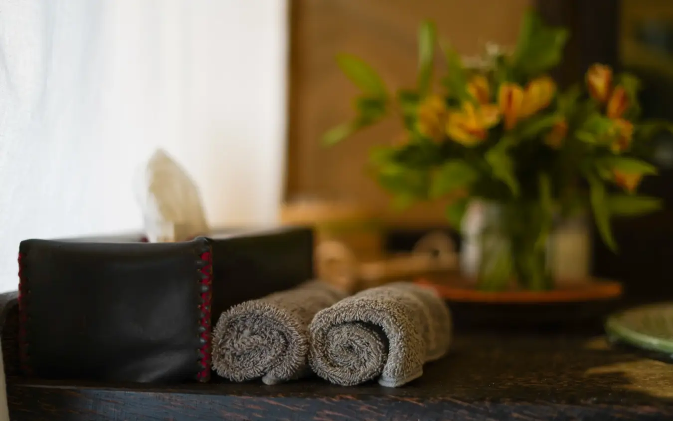 Rolled towels and tissue box on wooden bathroom counter with flowers, Roca River Camp, Maasai Mara, Kenya