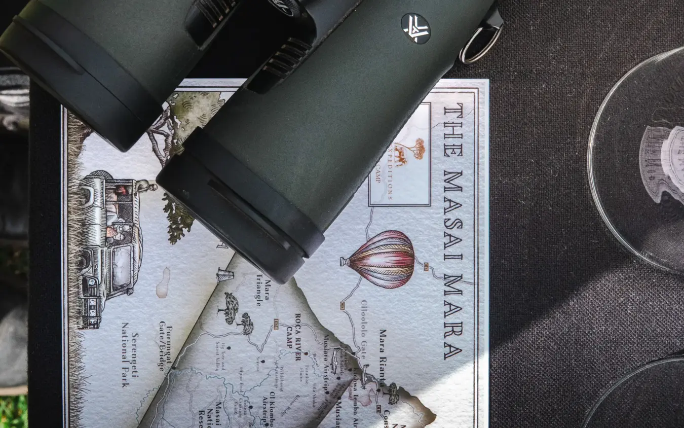 Binoculars and map laid on travel documents during safari planning, Roca River Camp, Maasai Mara, Kenya