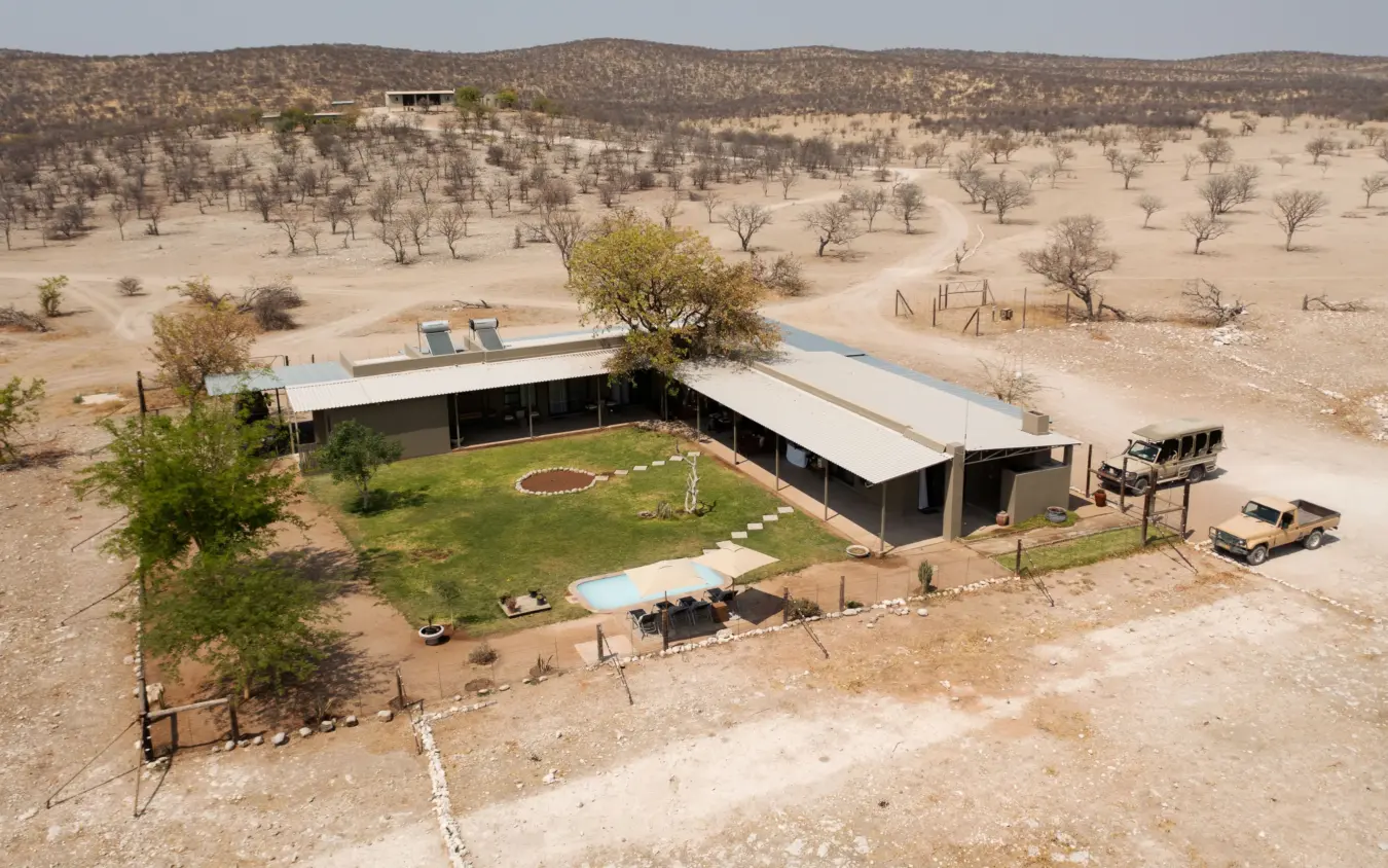 Modern lodge with green lawn and pool overlooking sparse bushveld landscape, Safari House, Etosha National Park, Namibia