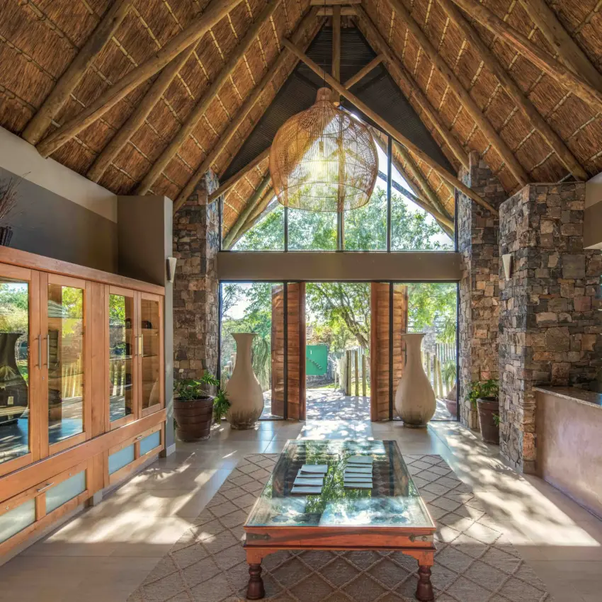 Luxury lodge interior with thatched roof and stone walls framing garden views, Safarihoek Lodge, Etosha National Park, Namibia