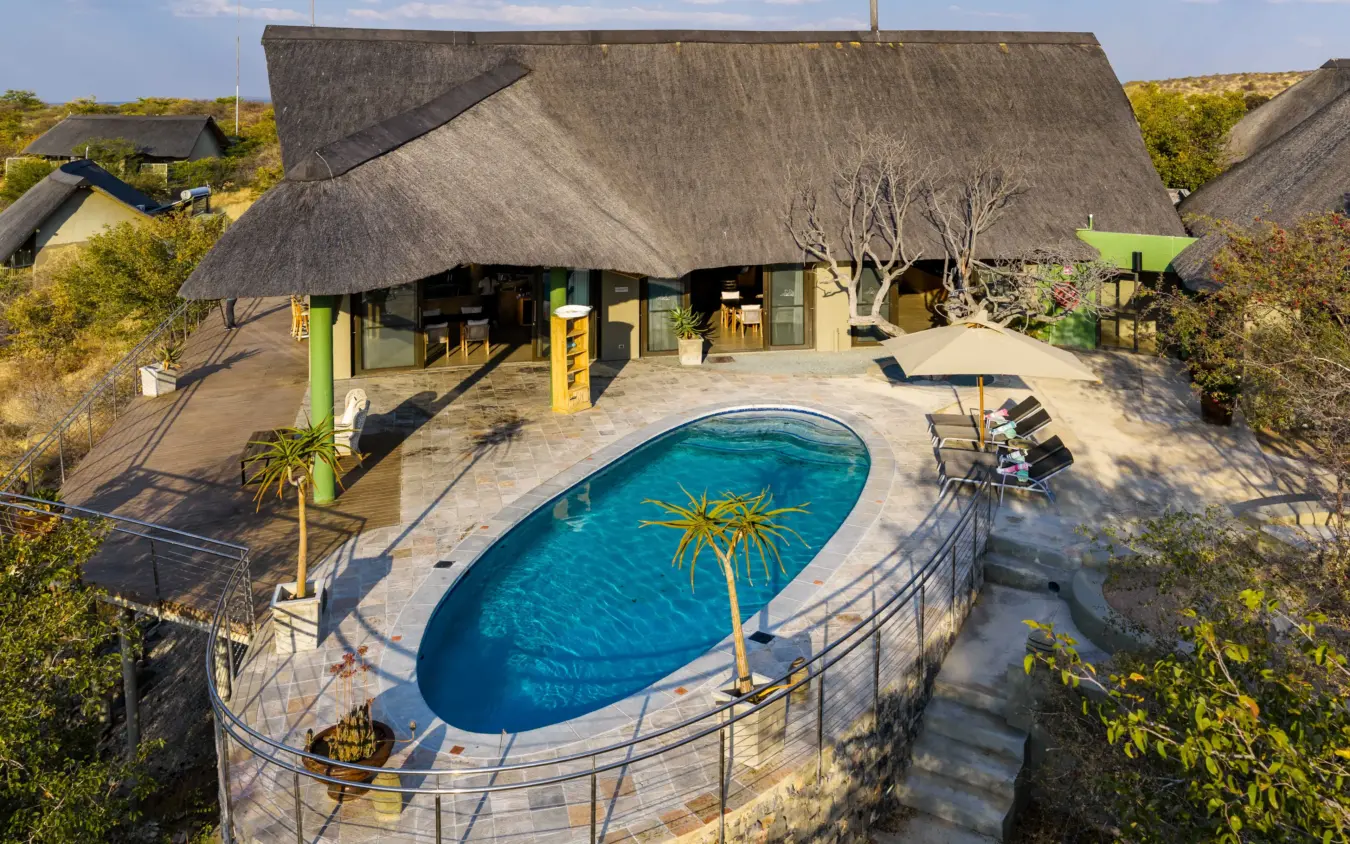Thatched-roof lodge with oval pool and wooden deck in bushland setting, Safarihoek Lodge, Etosha National Park, Namibia