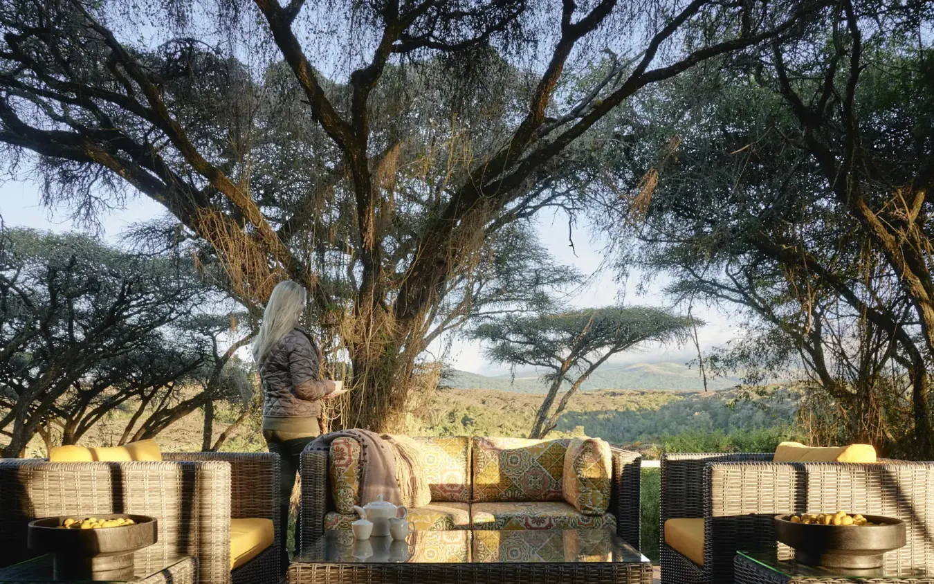 Guest viewing expansive savanna landscape from shaded terrace, Sanctuary Crater Camp, Ngorongoro Crater, Tanzania