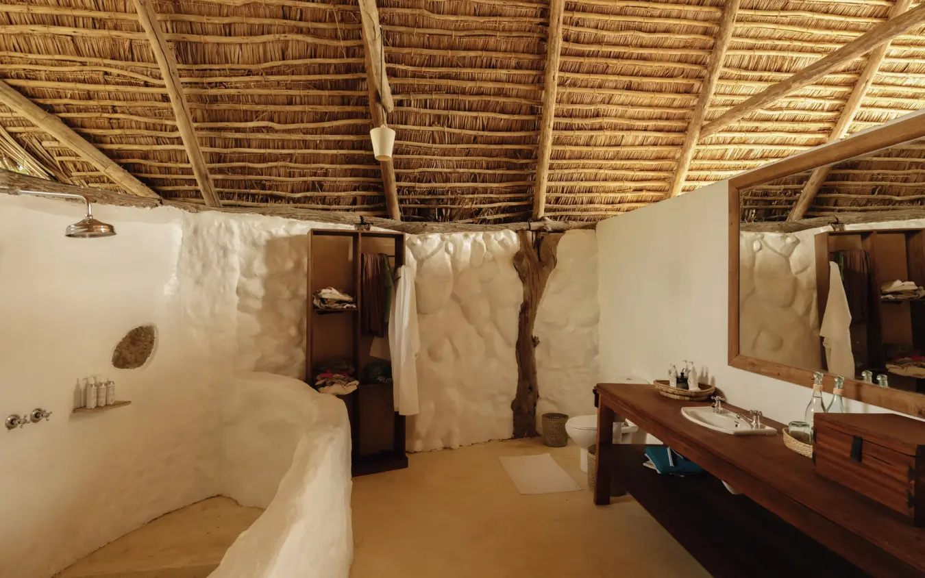 Luxury bathroom with curved stone bathtub and thatch roof interior, Sand Rivers, Nyerere National Park, Tanzania