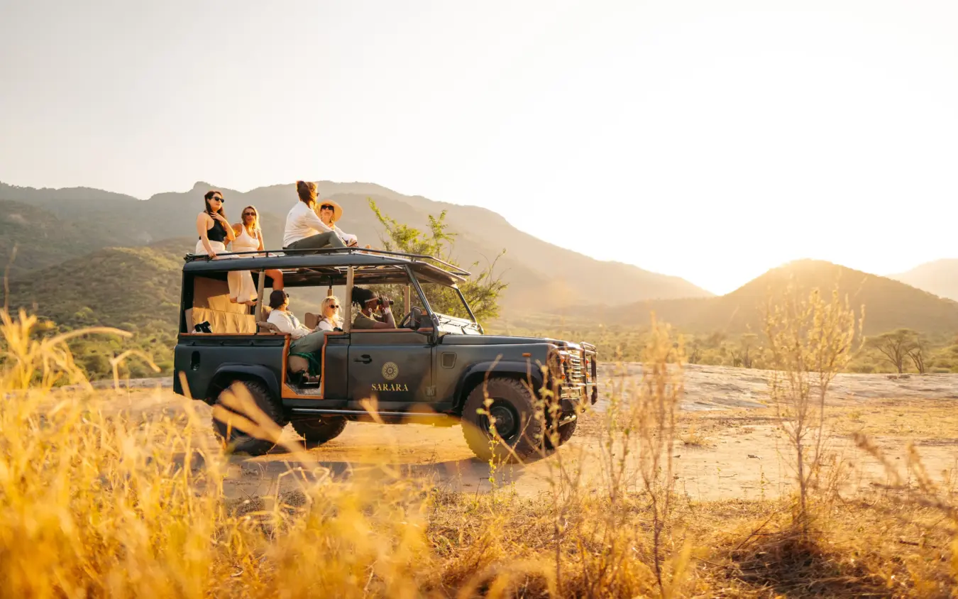 Safari vehicle packed with guests on open-air drive through arid valley landscape, Sarara Camp, Northern Kenya, Kenya