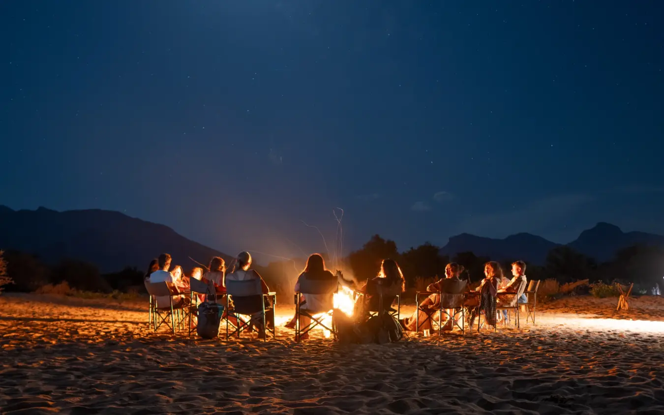 Group gathered around campfire on desert sand under starlit sky, Sarara Camp, Northern Kenya, Kenya