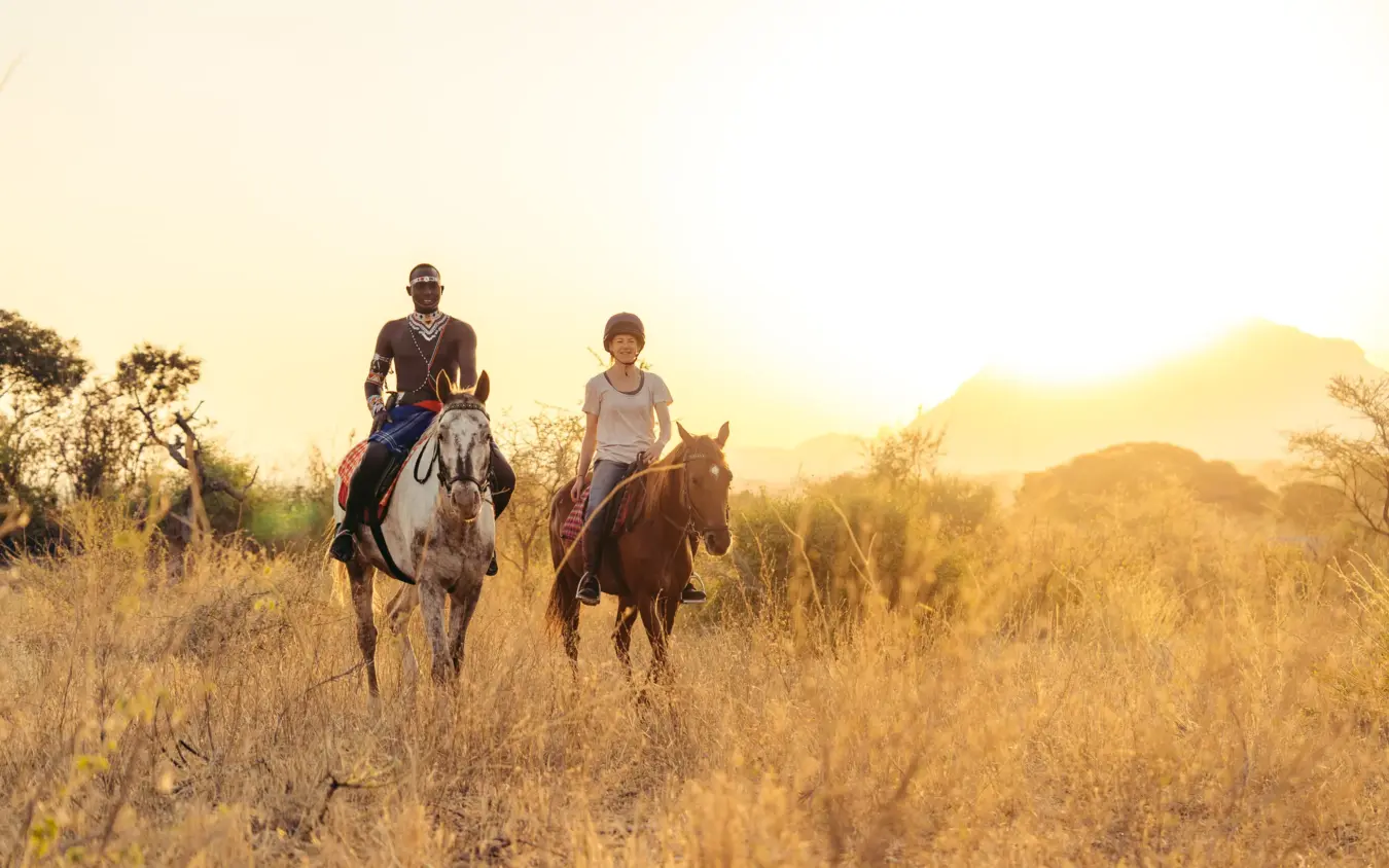 Couple horseback riding through dry grassland at golden hour, Sarara Camp, Northern Kenya, Kenya
