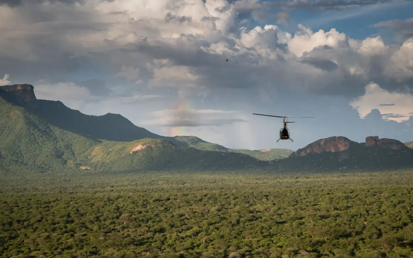 Helicopter flying over dense bushland with mountains in background, Sarara Camp, Northern Kenya, Kenya