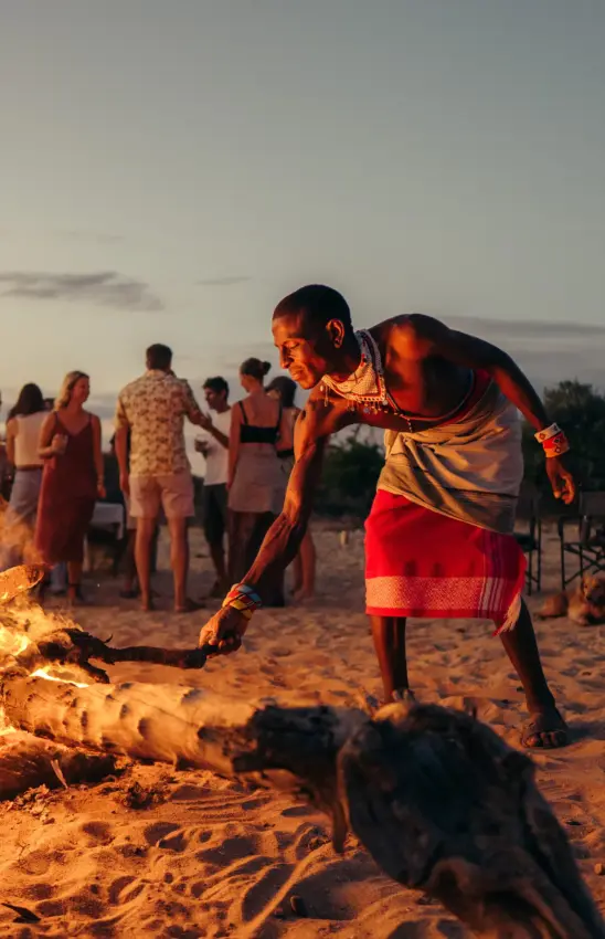 Man tending bonfire at beach gathering at sunset, Sarara Wilderness, Northern Kenya, Kenya