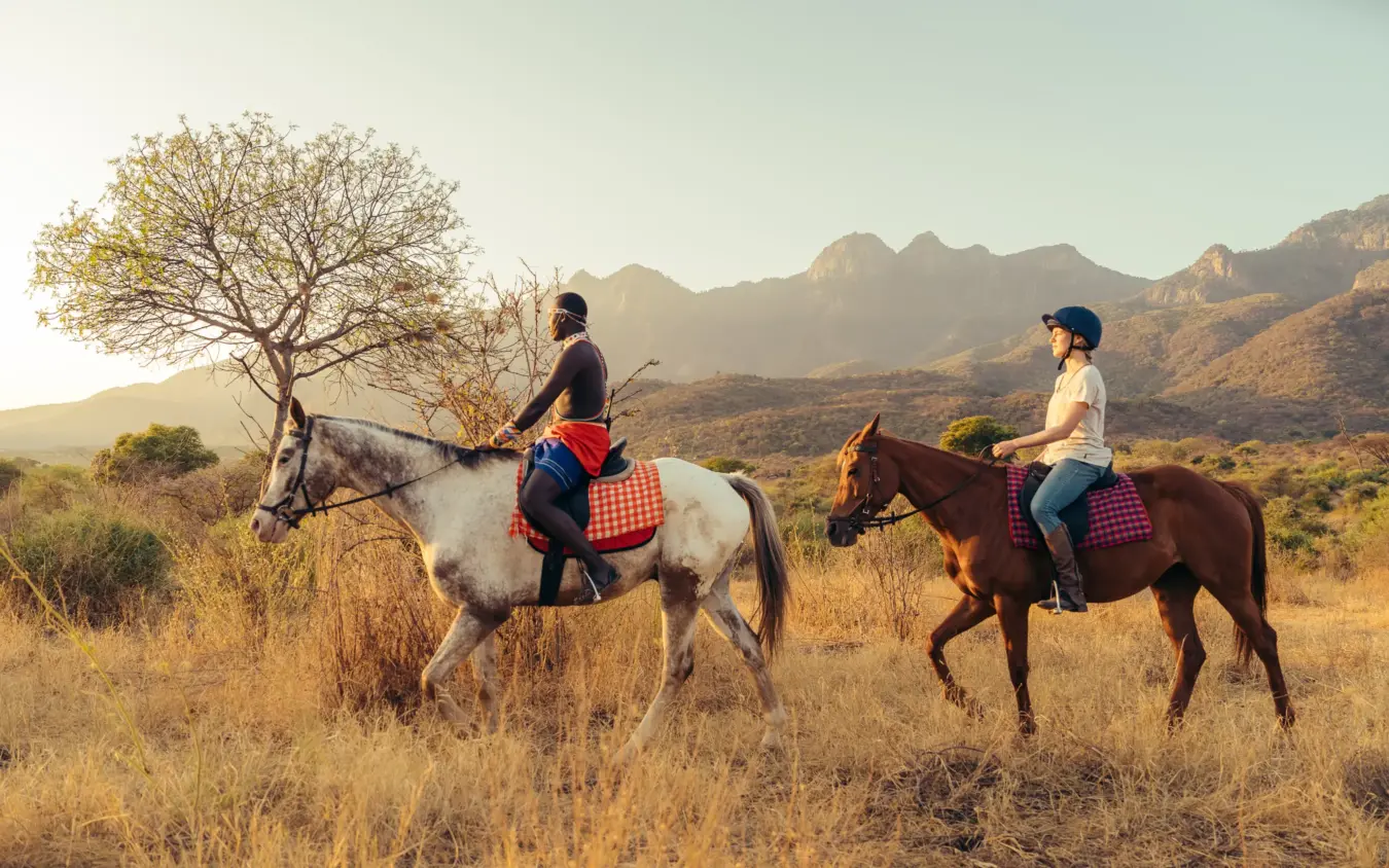 Horseback riders on scenic trail through arid savanna landscape with mountains, Sarara Wilderness, Northern Kenya, Kenya