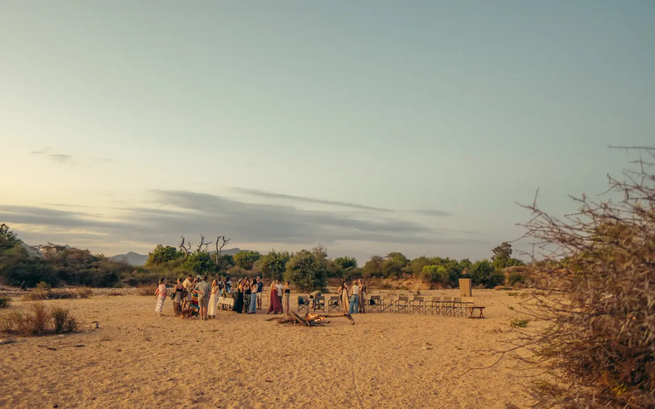 Group gathered at bush camp in golden grassland at dusk, Sarara Wilderness, Northern Kenya, Kenya