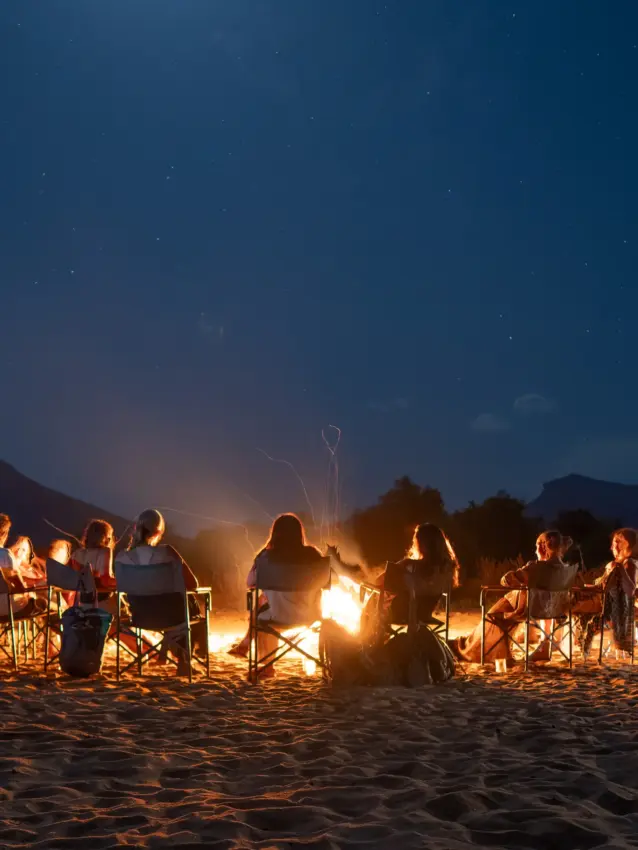 Group of people sitting around beach bonfire at night under starry sky, Sarara Wilderness, Northern Kenya, Kenya