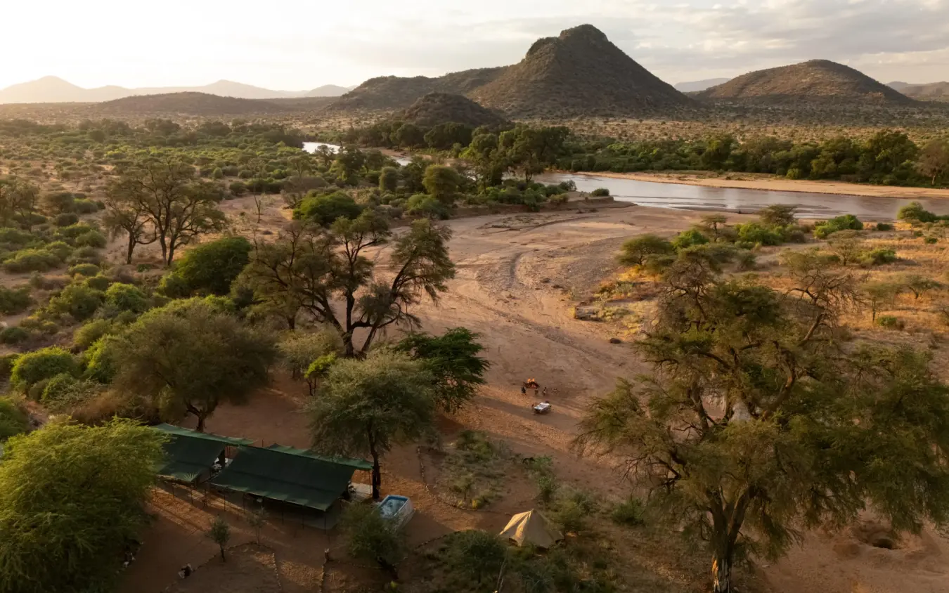 Safari camp on riverbank with acacia trees and distant mountains, Sarara Wilderness, Northern Kenya, Kenya