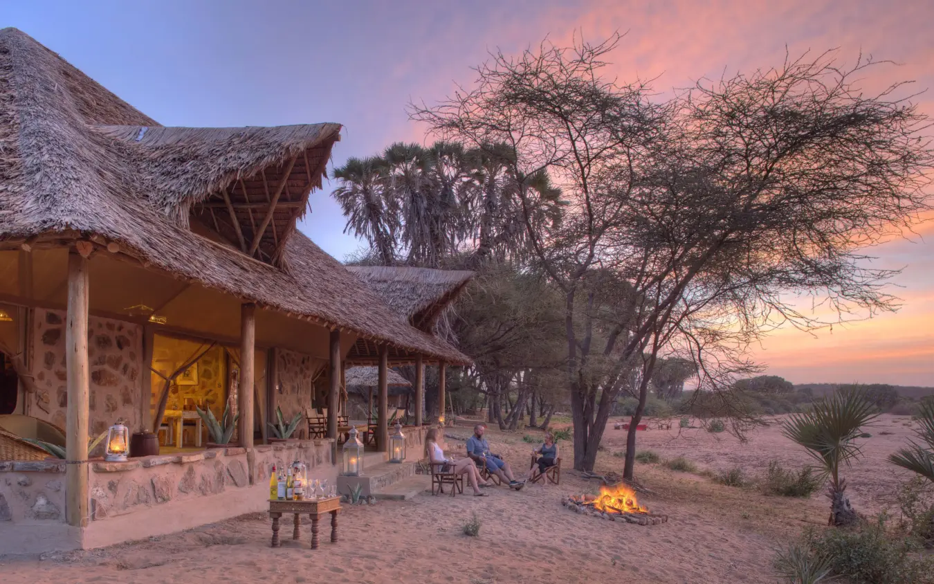 Guests around campfire at thatched lodge at sunset, Saruni Rhino, Northern Kenya, Kenya