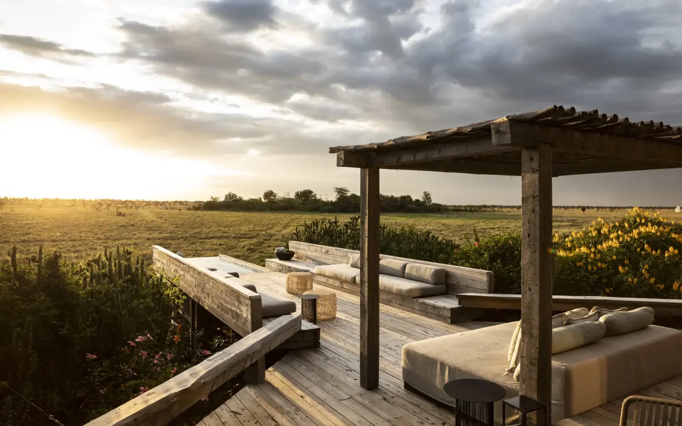 Wooden deck with daybed seating overlooking vast grassland at sunset, Segera, Laikipia Highlands, Kenya