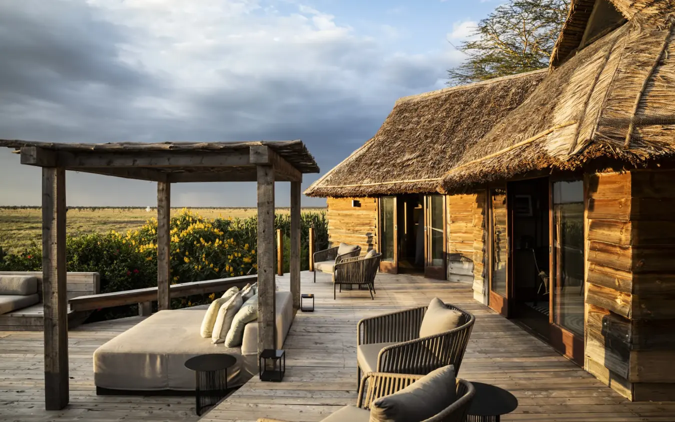 Thatched lodge accommodation with deck seating overlooking vast grassland plains, Segera, Laikipia Highlands, Kenya