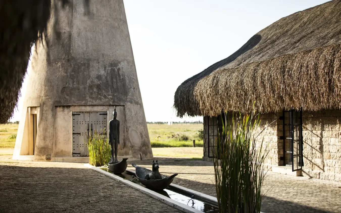 Thatched-roof lodge buildings with stone courtyard and open grassland beyond, Segera, Laikipia Highlands, Kenya