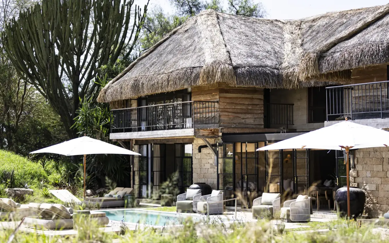 Luxury thatched-roof lodge with pool terrace and white umbrellas overlooking gardens, Segera, Laikipia Highlands, Kenya