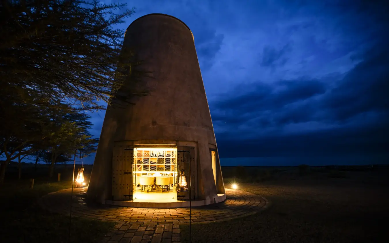 Illuminated cylindrical structure with dining setup at dusk in open landscape, Segera, Laikipia Highlands, Kenya