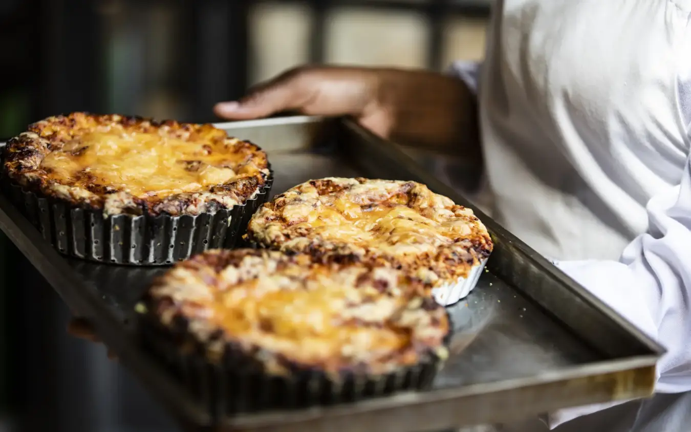 Baker holding freshly baked custard tarts on metal tray, Segera, Laikipia Highlands, Kenya