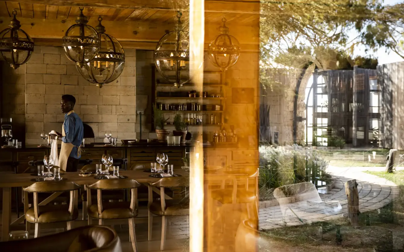 Lodge interior with bar seating and courtyard garden view through open doors, Segera, Laikipia Highlands, Kenya