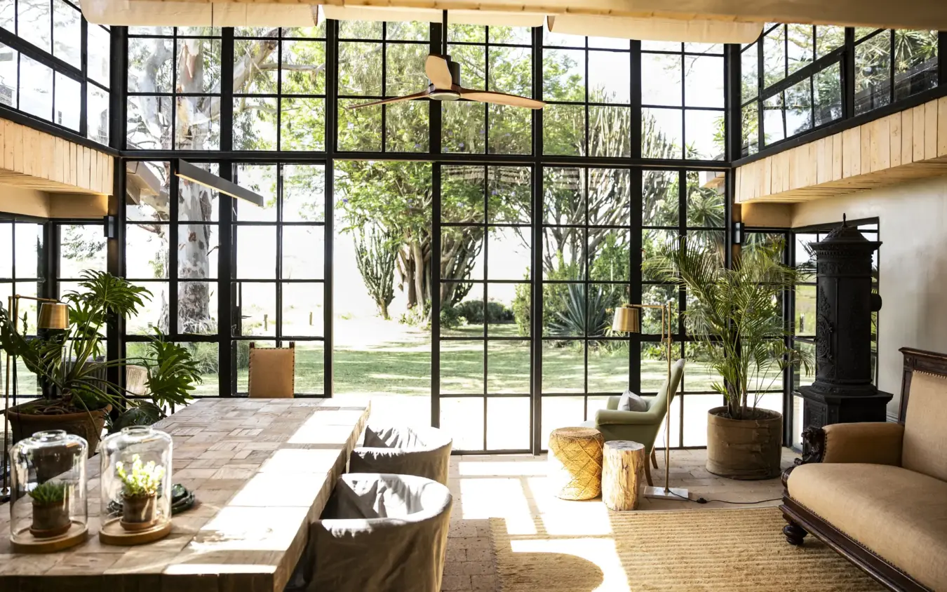 Modern interior lounge with floor-to-ceiling windows overlooking manicured gardens, Segera, Laikipia Highlands, Kenya