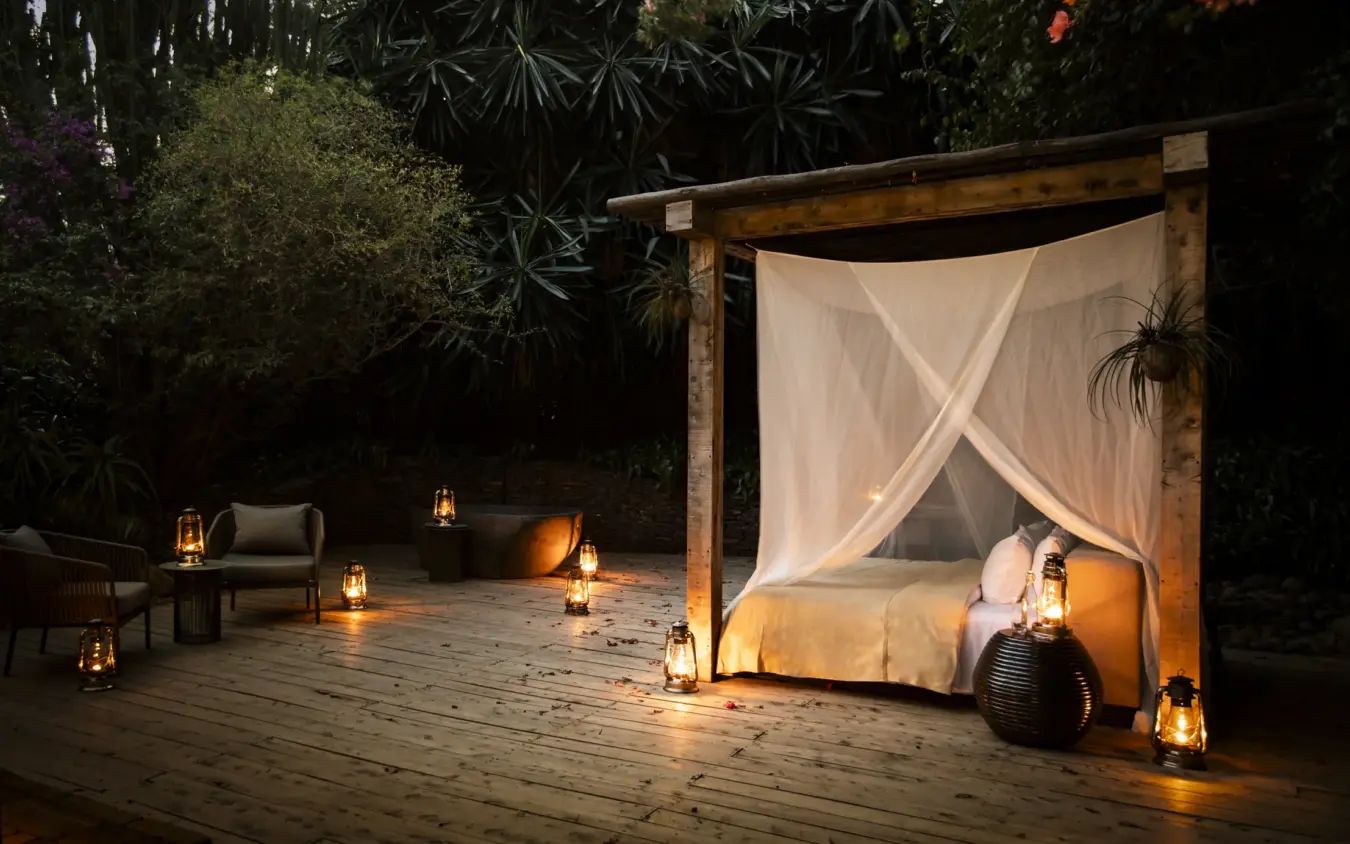 Outdoor bedroom with canopy bed and lanterns on wooden deck at night, Segera, Laikipia Highlands, Kenya