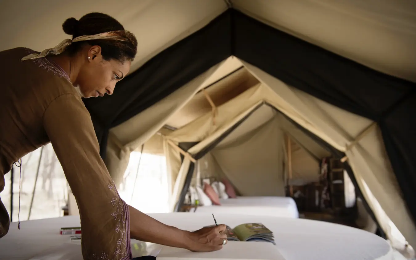Woman painting at table inside canvas safari tent, Serian Serengeti Mobile Kusini, Serengeti National Park, Tanzania