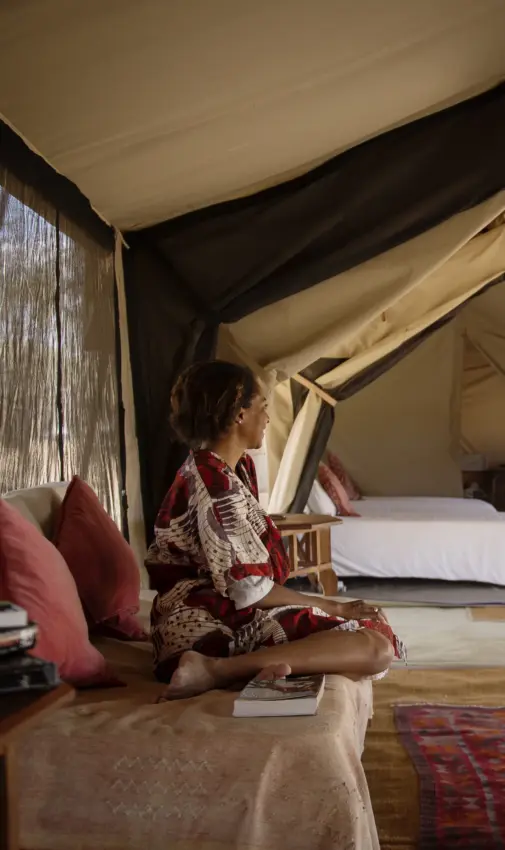 Woman relaxing on bed in canvas safari tent interior, Serian Serengeti Mobile Kusini, Serengeti National Park, Tanzania