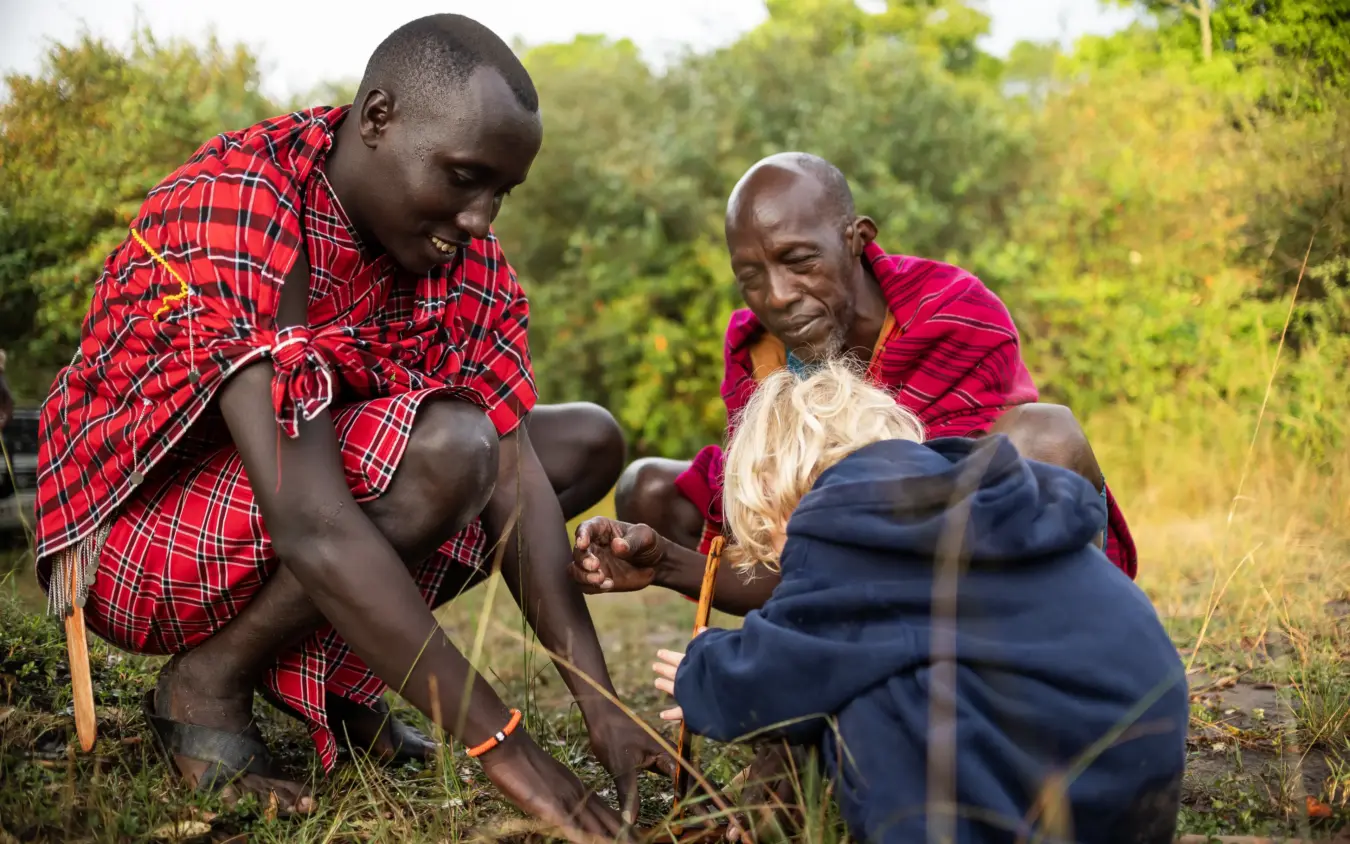 Local guides demonstrating traditional fire-making technique in grassland, Seringet Mara Camp, Maasai Mara, Kenya