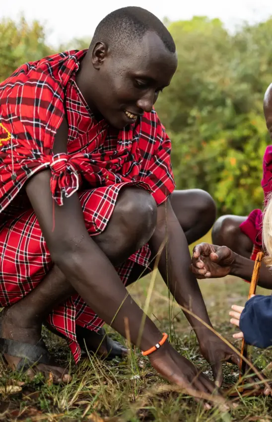 Young person in red plaid shirt planting seedling in garden with others, Seringet Mara Camp, Maasai Mara, Kenya