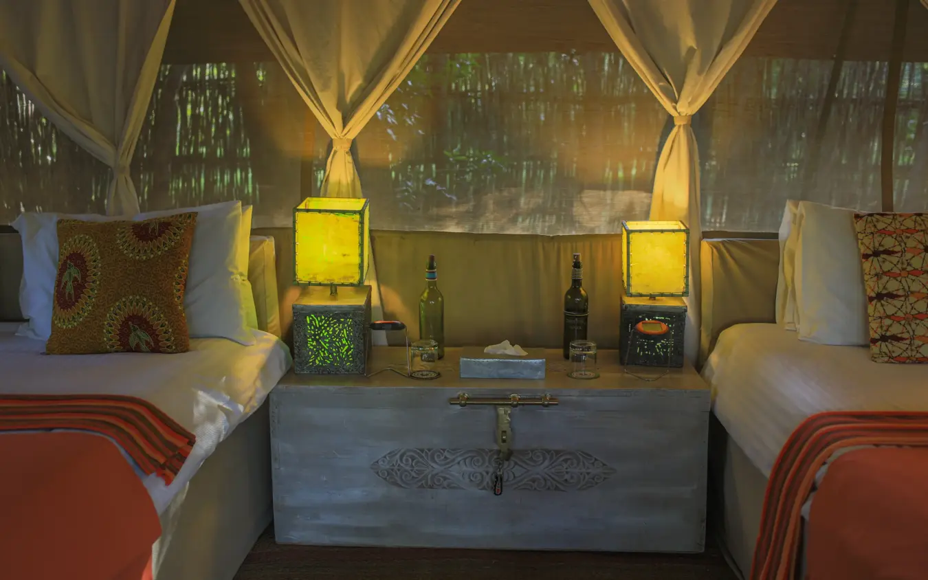 Twin beds in luxury tent with draped fabric and lanterns, Speke’s Camp, Maasai Mara, Kenya