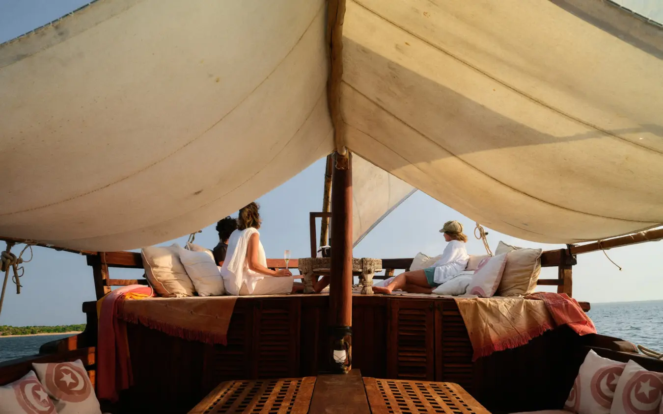 Wooden dhow with canvas canopy and guests relaxing on deck overlooking ocean, The Cabanas, Lamu Archipelago, Kenya