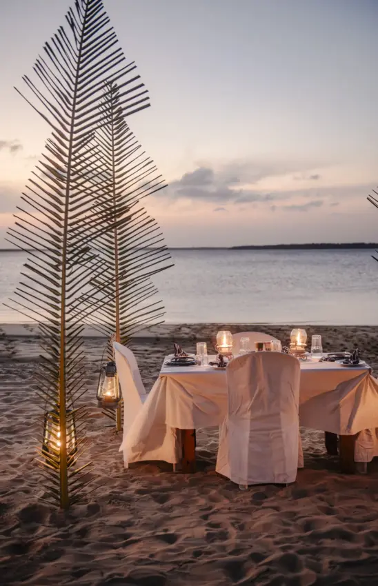 Beachfront dinner table with palm leaf decoration at sunset, The Cabanas, Lamu Archipelago, Kenya