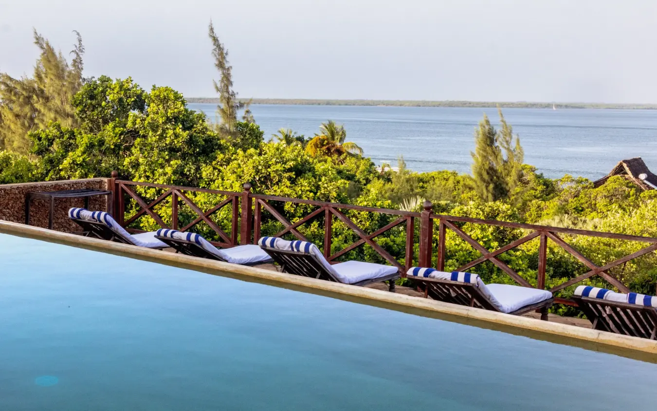 Loungers with striped cushions by infinity pool overlooking coastal bay, The Cabanas, Lamu Archipelago, Kenya