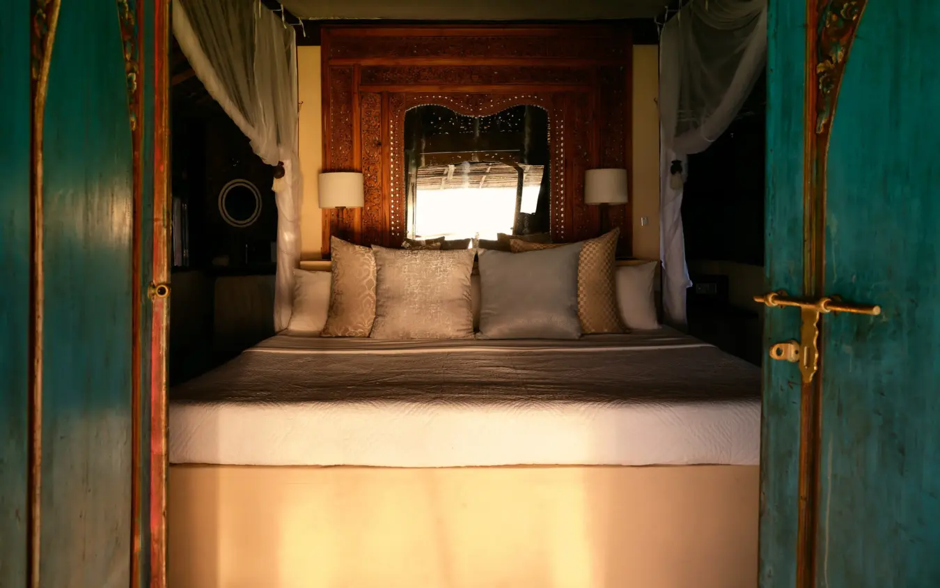 Luxury bedroom interior with turquoise doors and decorated wooden headboard, The Cabanas, Lamu Archipelago, Kenya
