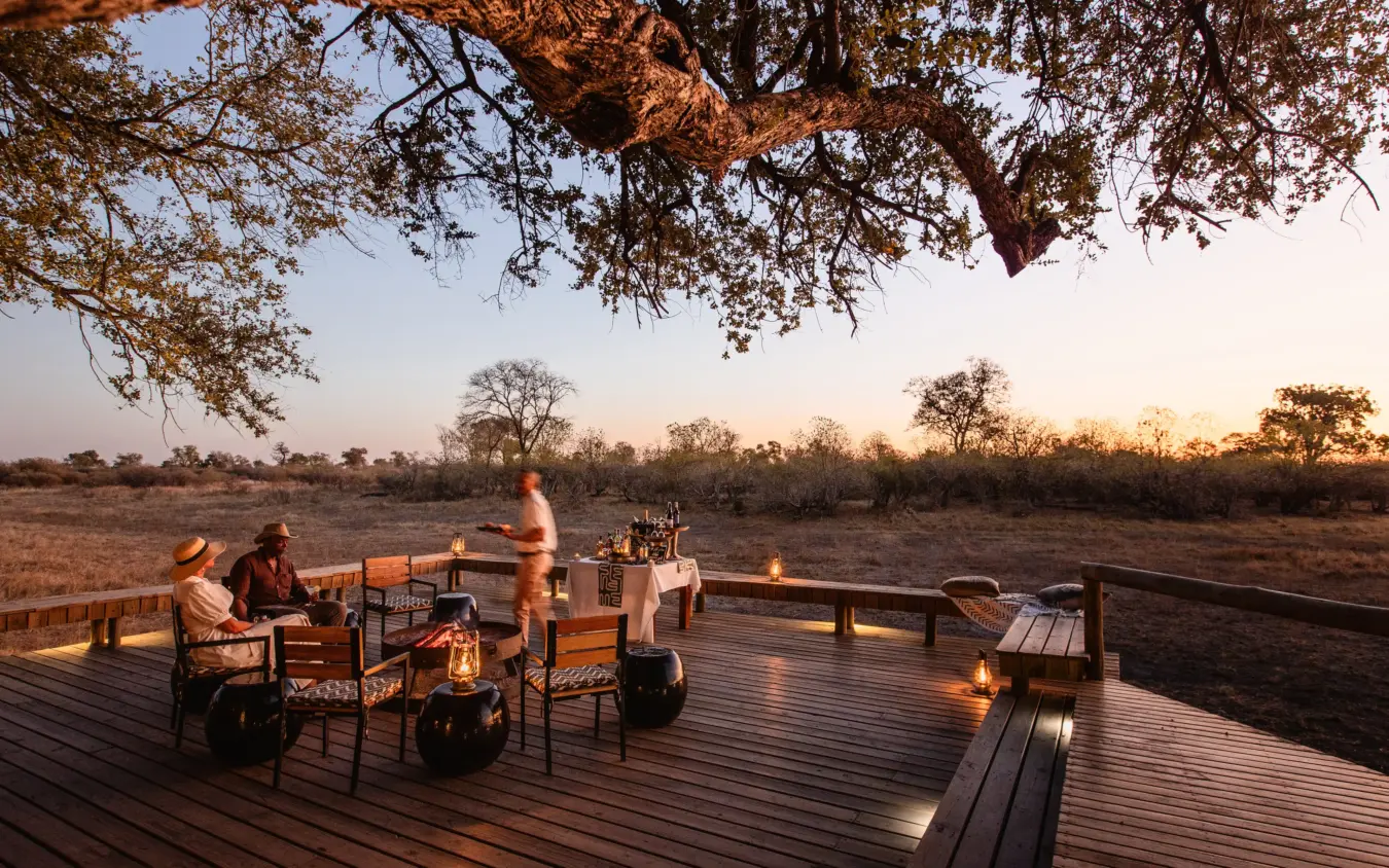 Guests dining on wooden deck at sunset overlooking savanna landscape, Savuti Camp, Linyanti Wildlife Reserve, Botswana