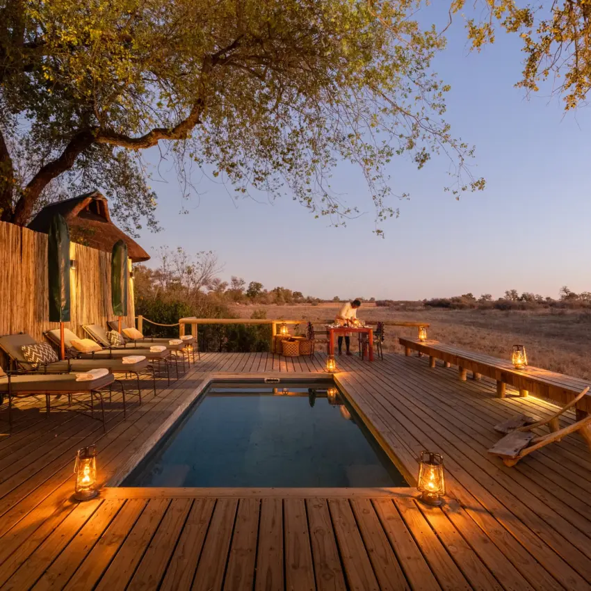 Wooden deck with illuminated pool overlooking vast savanna landscape at dusk, Savuti Camp, Linyanti Wildlife Reserve, Botswana