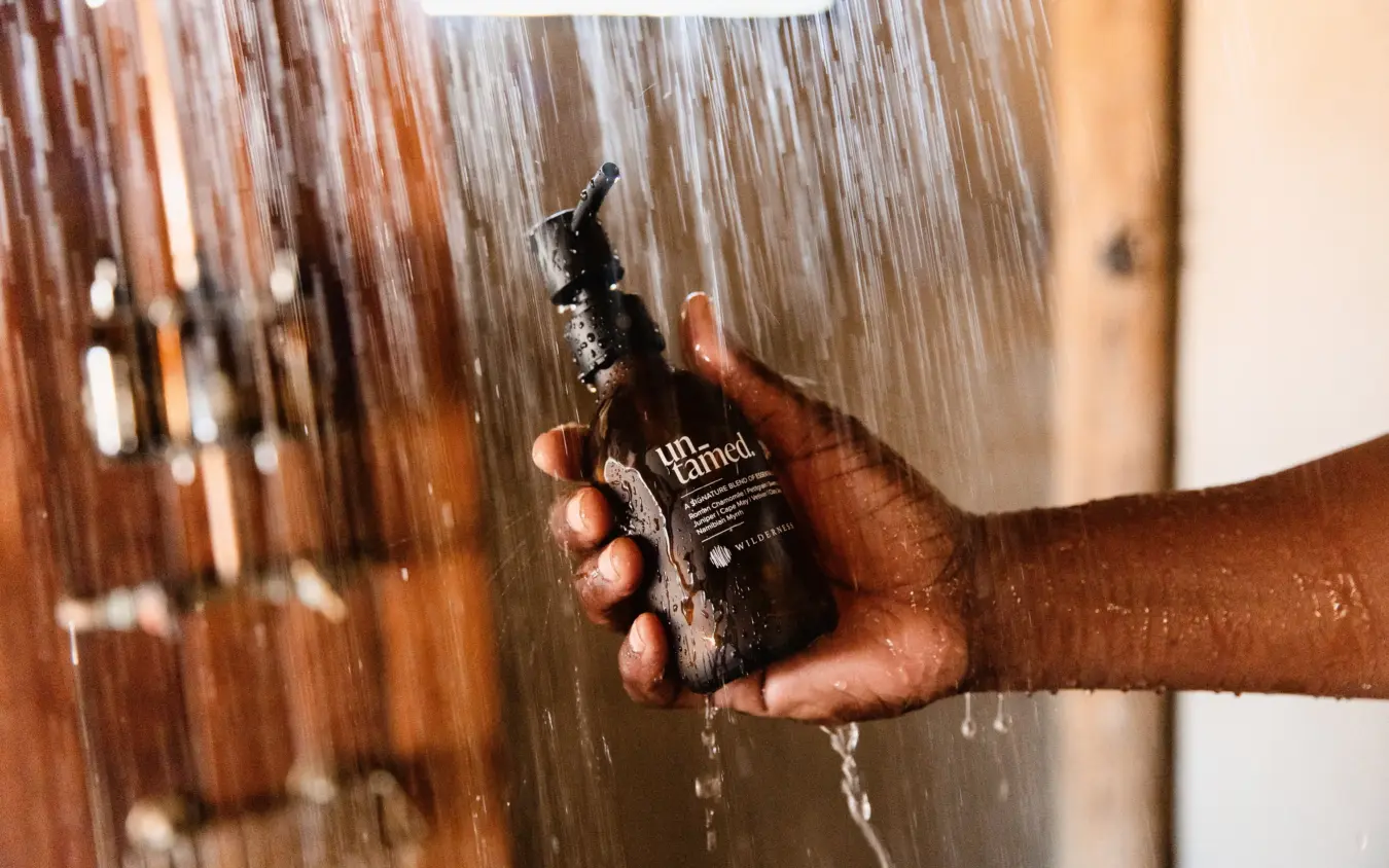 Hand holding toiletry bottle under running shower water, Savuti Camp, Linyanti Wildlife Reserve, Botswana