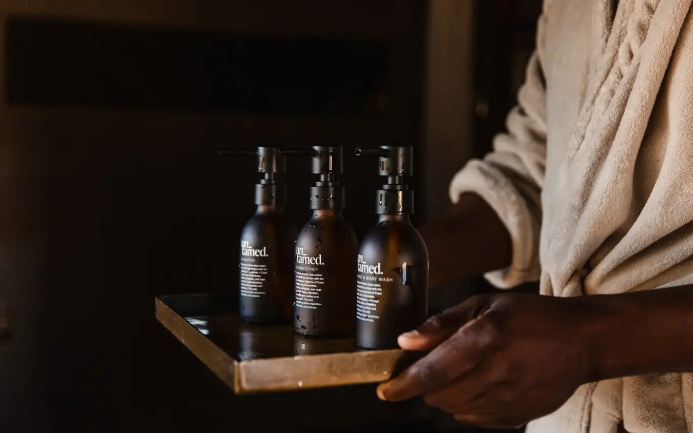 Person holding wooden tray with three dark glass bottles of skincare products, Savuti Camp, Linyanti Wildlife Reserve, Botswana