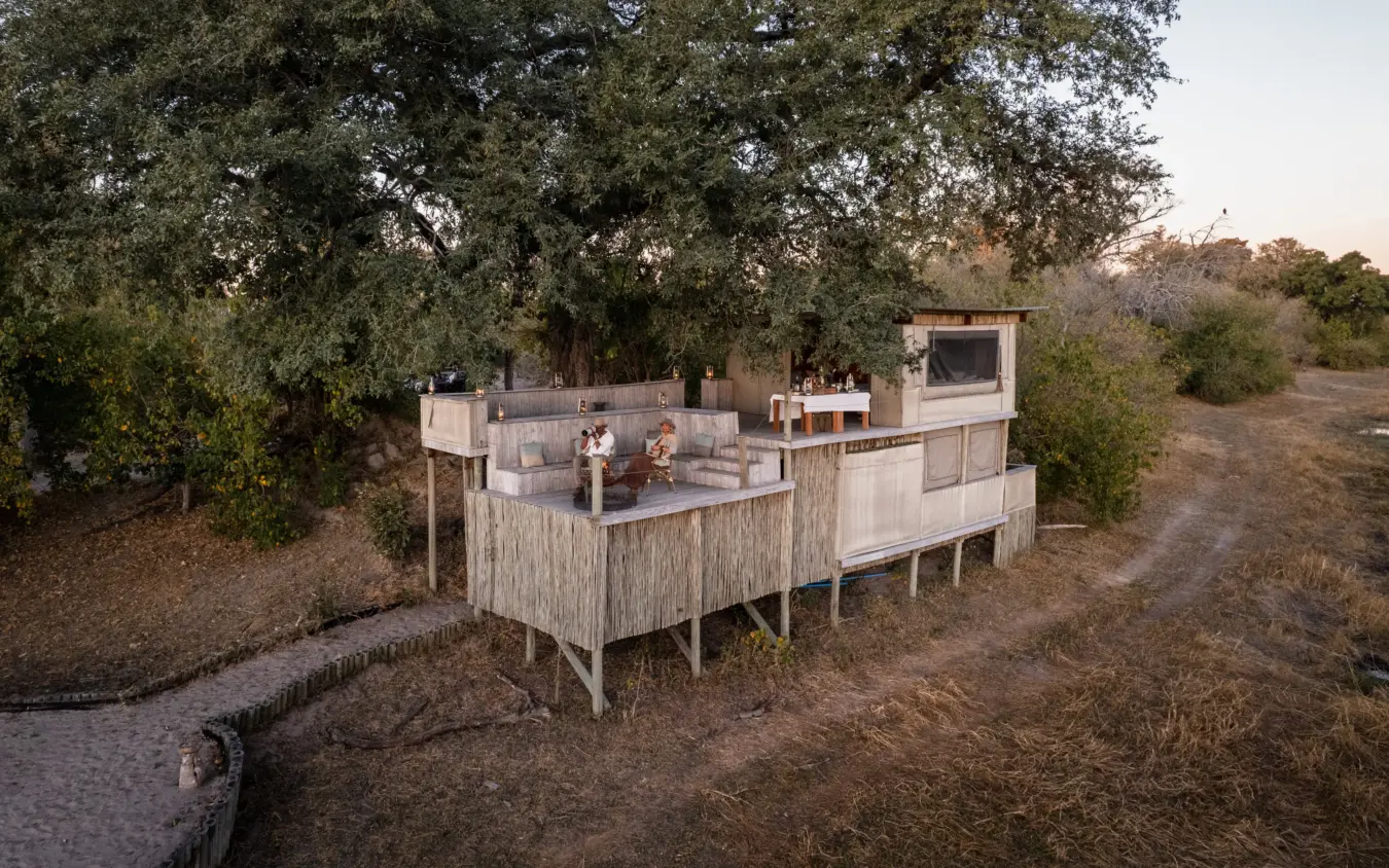 Elevated safari lodge with thatched panels overlooking dry bushland at dusk, Savuti Camp, Linyanti Wildlife Reserve, Botswana