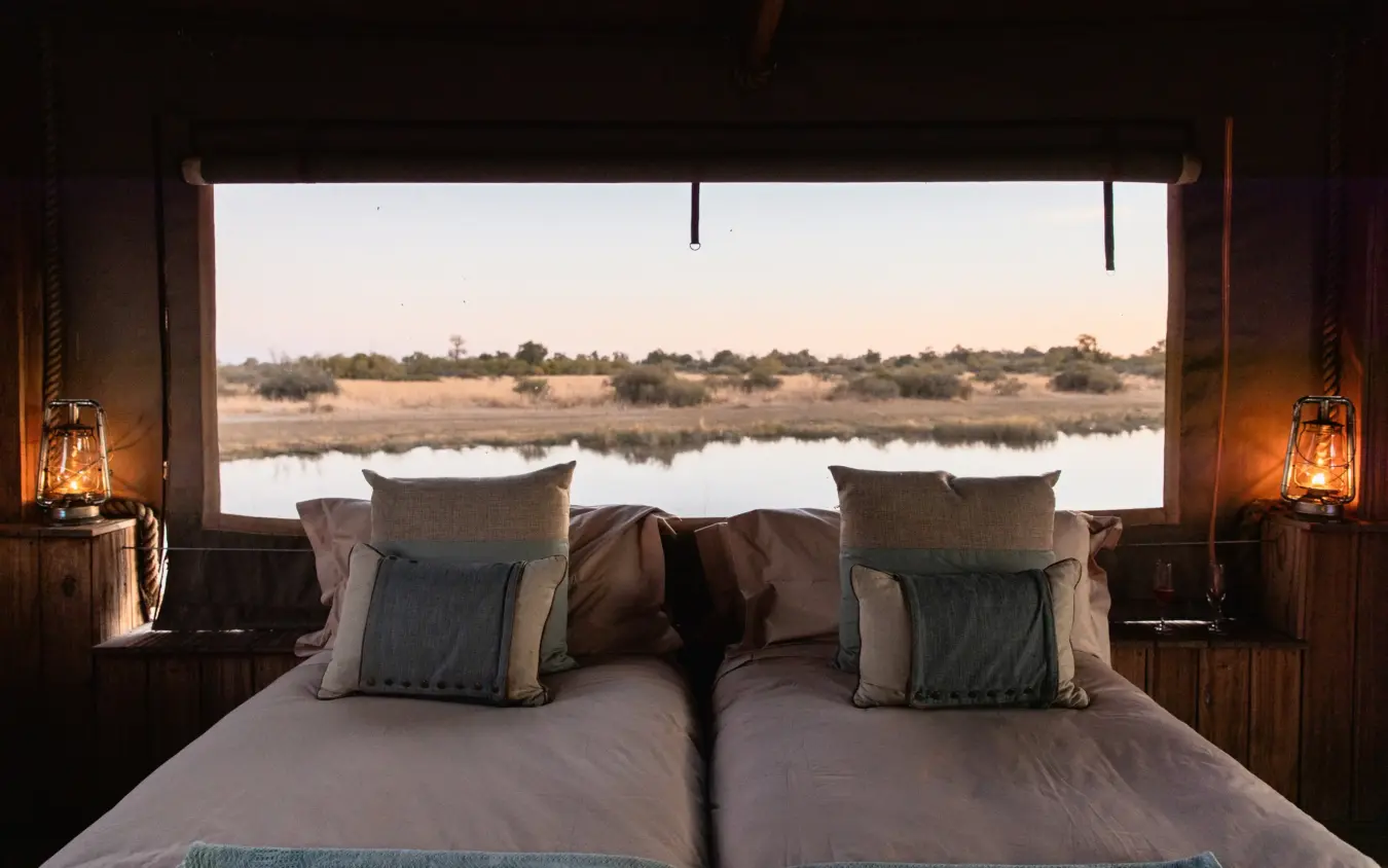 Bed with river view through large windows at sunrise, Savuti Camp, Linyanti Wildlife Reserve, Botswana