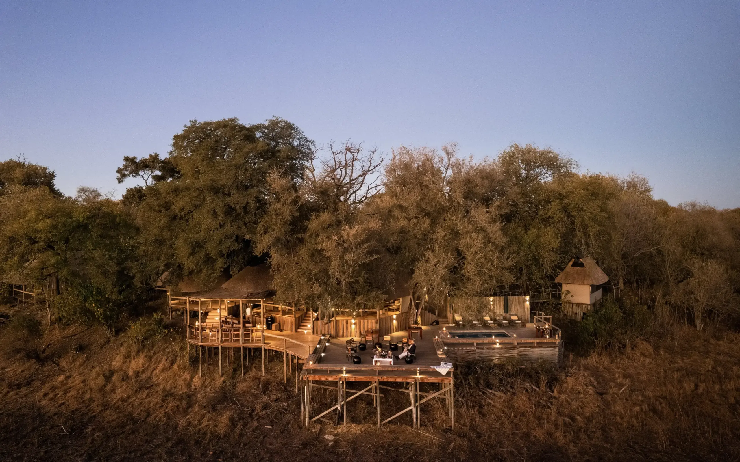 Elevated wooden lodge structures among ancient trees in dry landscape, Savuti Camp, Linyanti Wildlife Reserve, Botswana